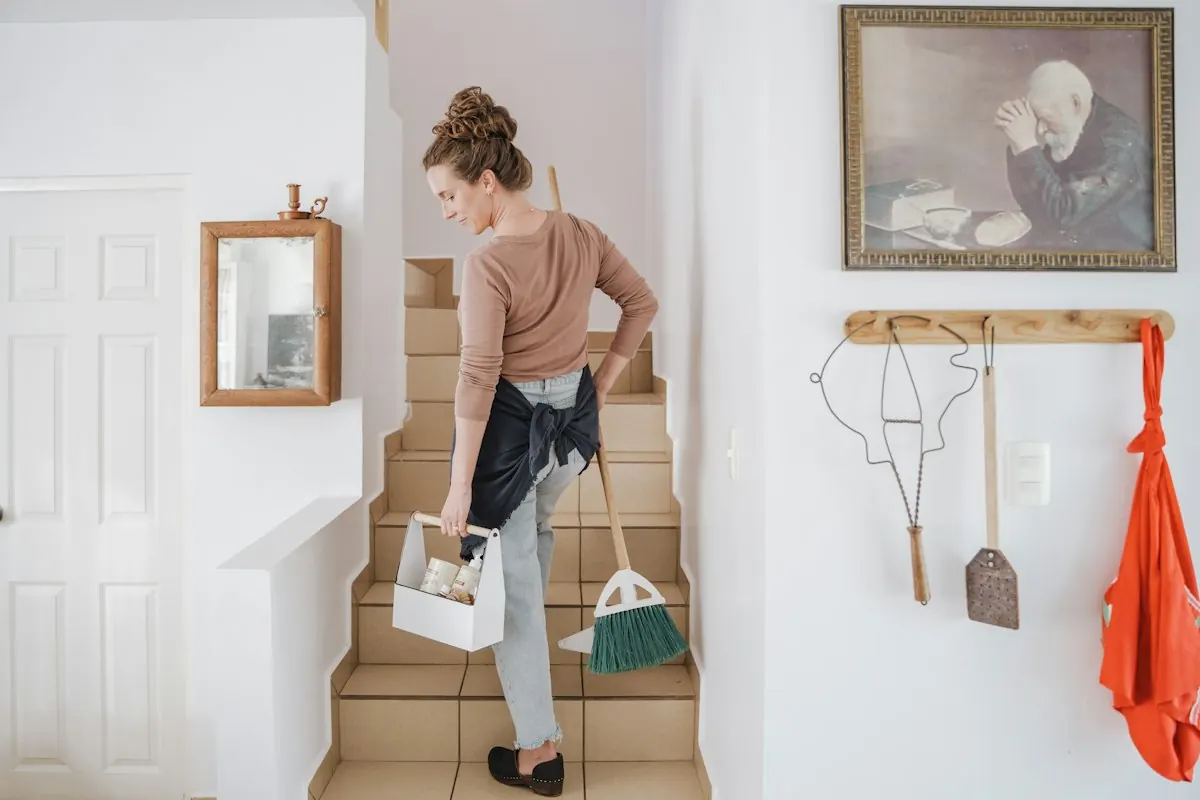 A cleaner carrying her caddy and equipment up the stairs of a home